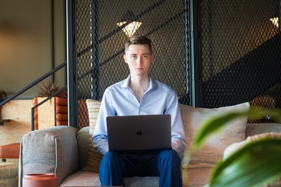 woman in white shirt sitting on couch using macbook